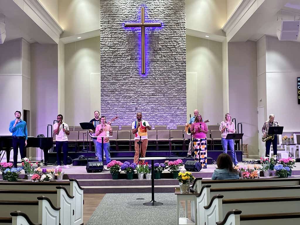 Brightly lit stage inside New Albany United Methodist Church with a group of singers and musicians p.